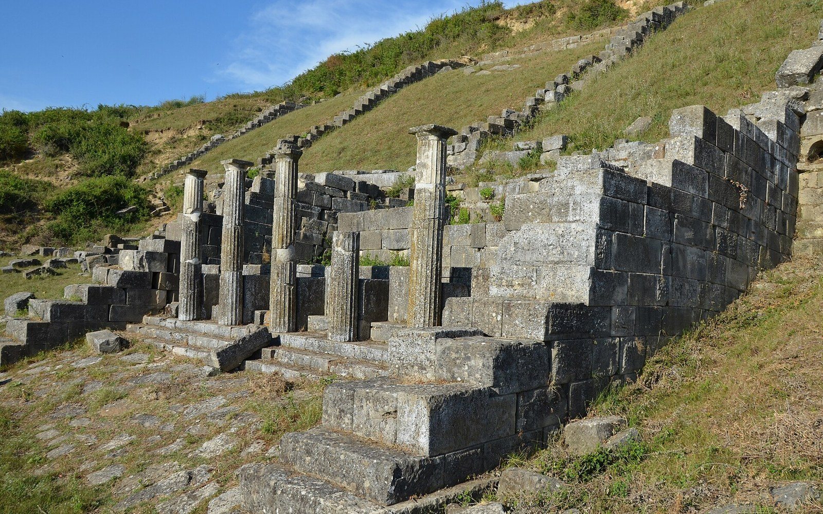A row of standing columns and stepped stonework on a grassy hillside