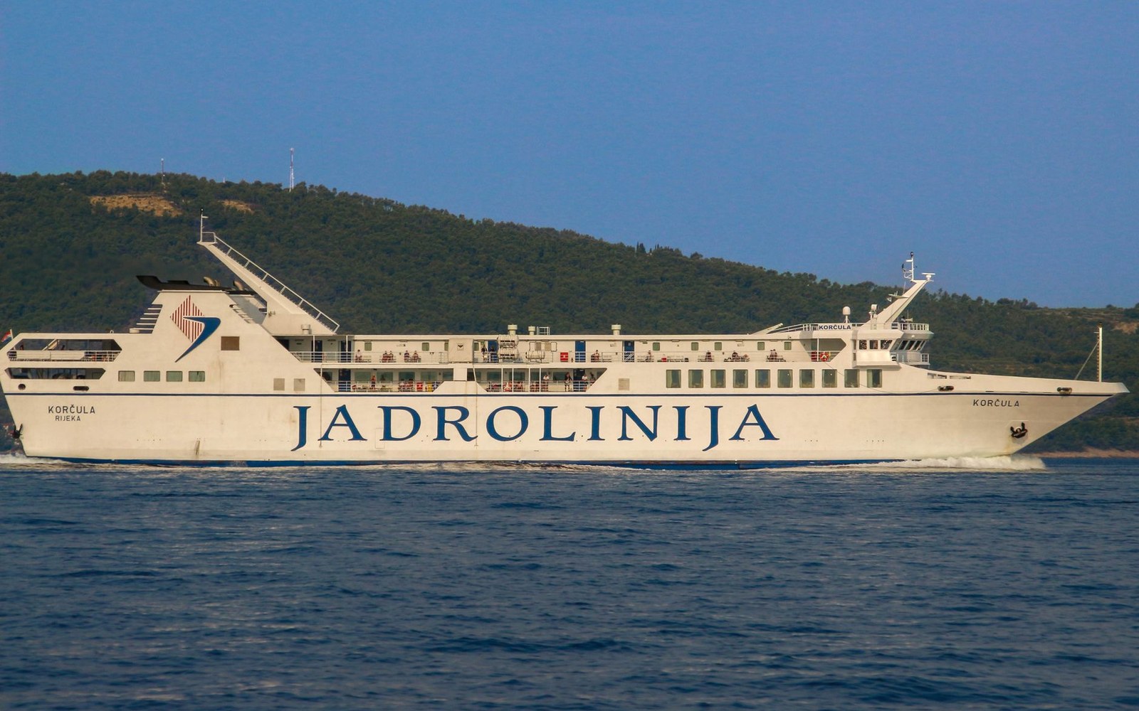 A car ferry under way on flat water with a wooded shore behind
