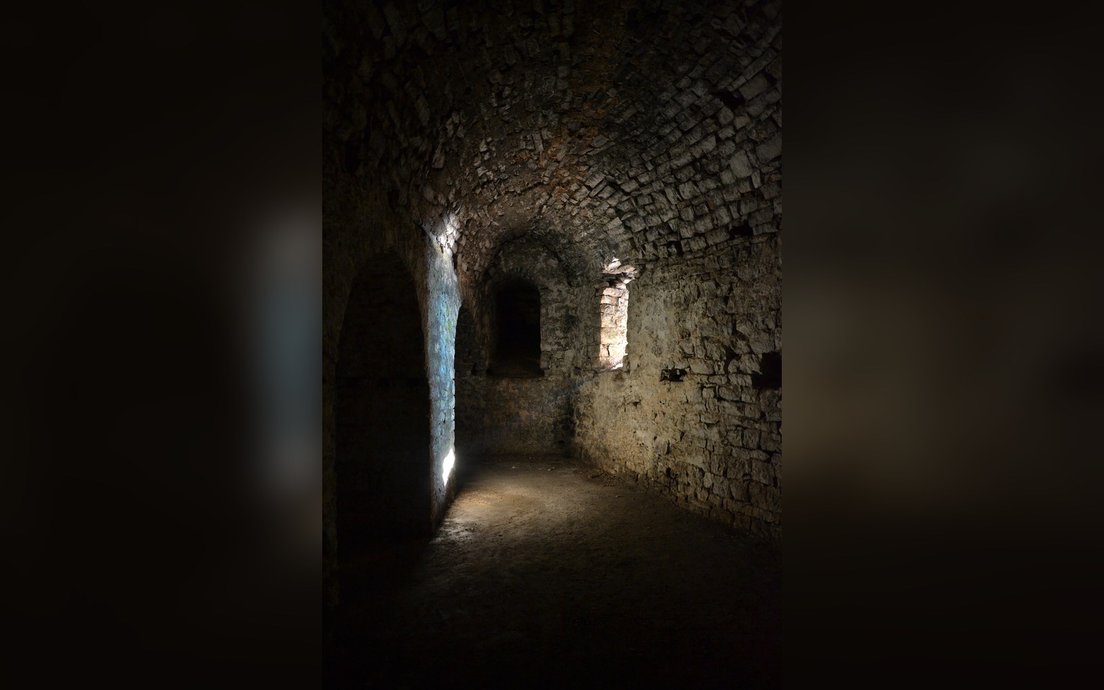 A barrel-vaulted stone corridor inside a coastal fortress, lit by a single embrasure